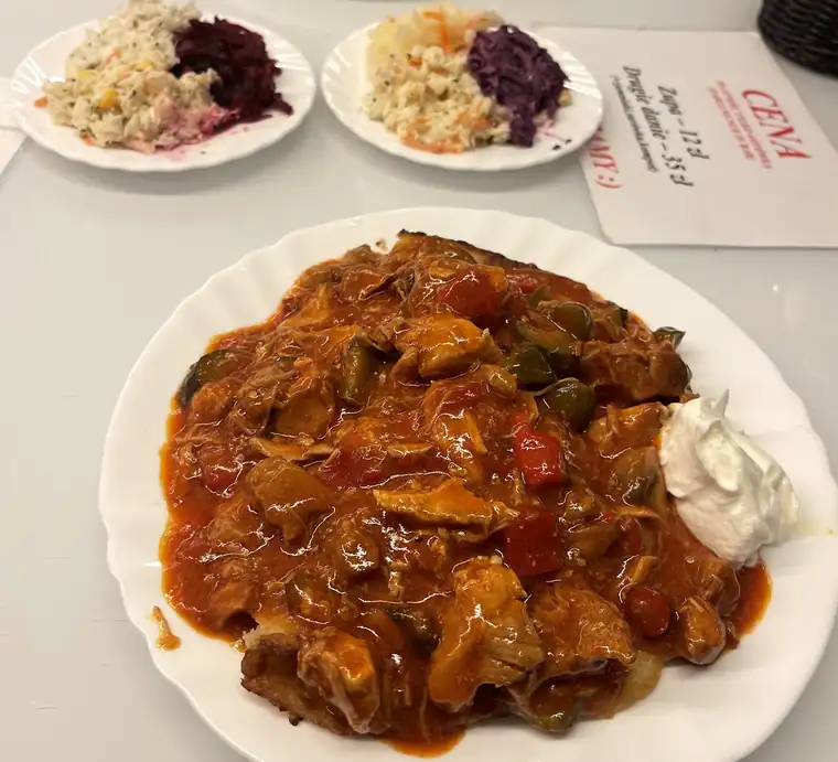 Mięso w sosie na dużym białym talerzu, obok surówki